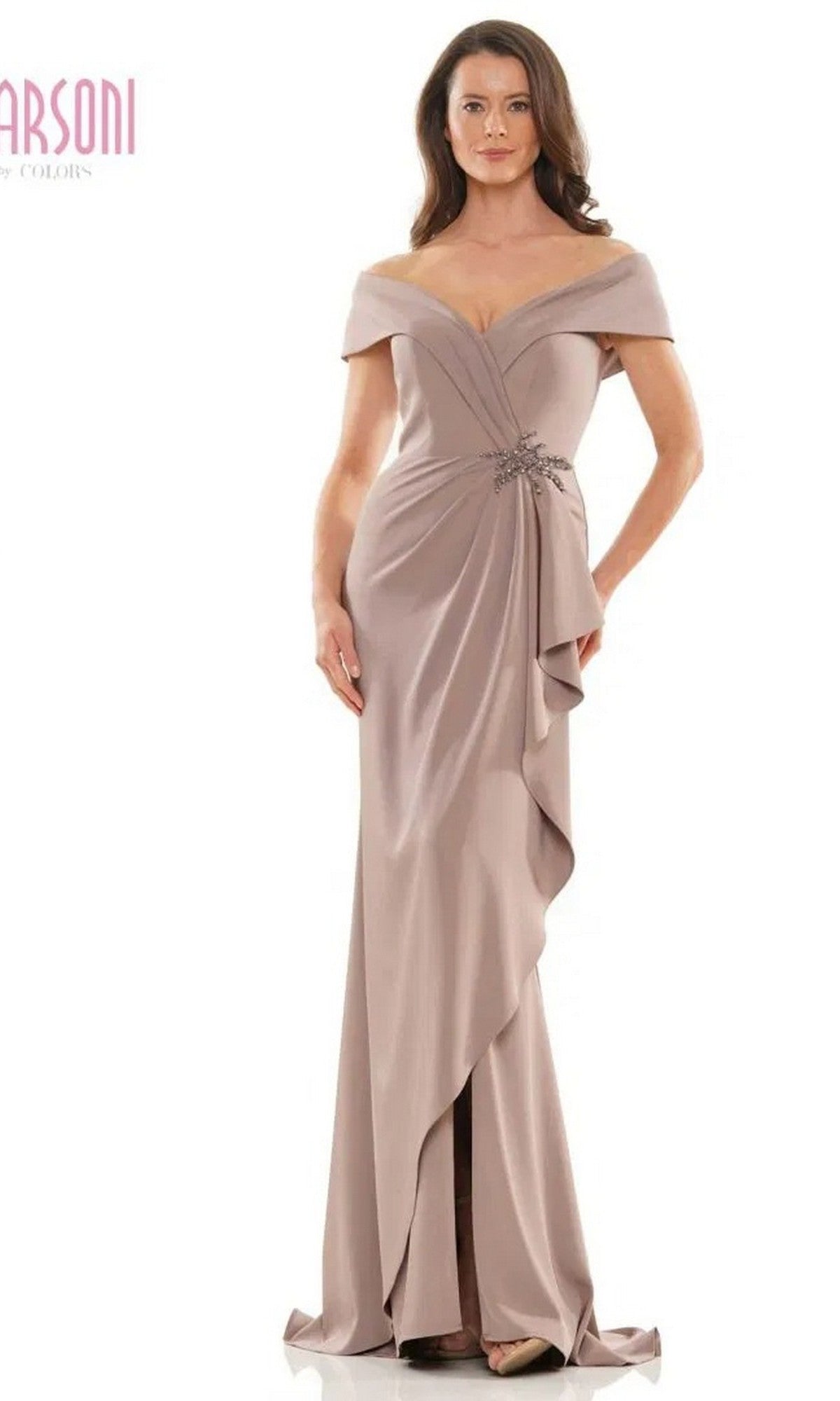 A woman wears the Marsoni MV1180 long formal dress in mink, featuring an off-the-shoulder neckline, floor-length draped design, gathered details, and a sparkling beaded waistline.